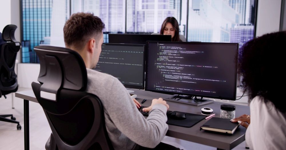 Zwei Entwickler an Bildschirmen mit Programmcode in einem Büro