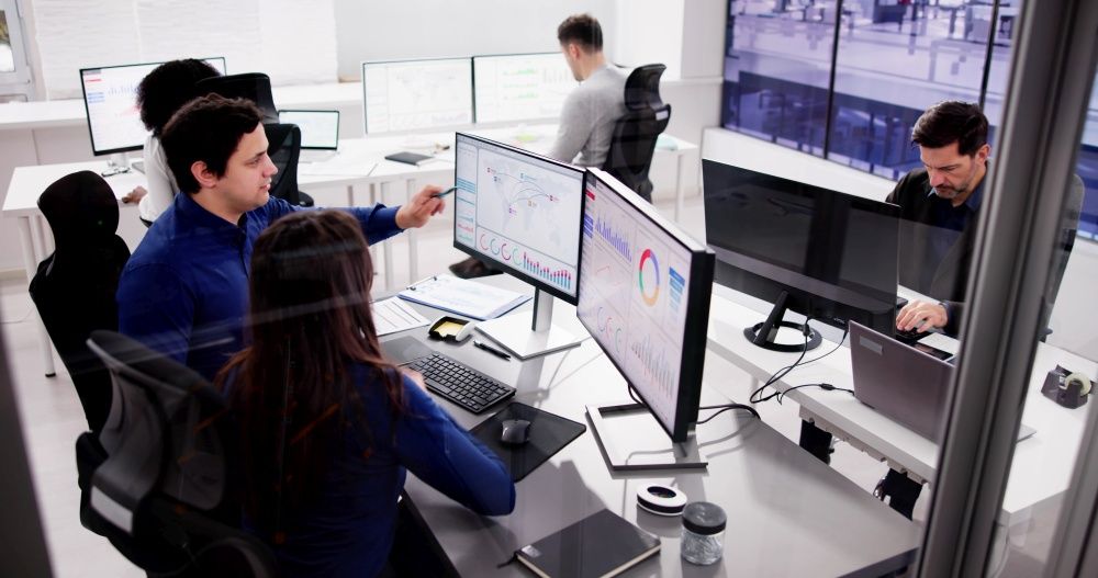 Mehrere Mitarbeiter in einem Service Center vor Bildschirmen mit Auswertungen und einer Monitorwand